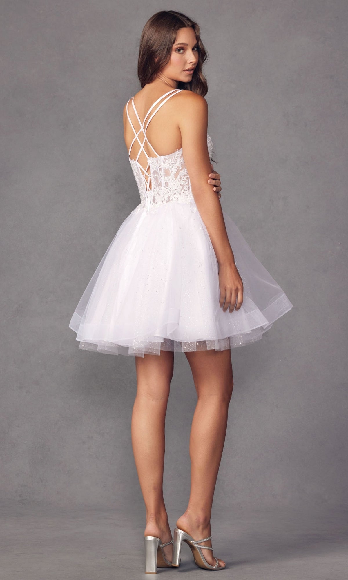 A woman poses against a gray background, facing away, wearing the Sheer-Bodice Short A-Line Prom Dress 883 featuring a corset-style bodice and crisscross straps.